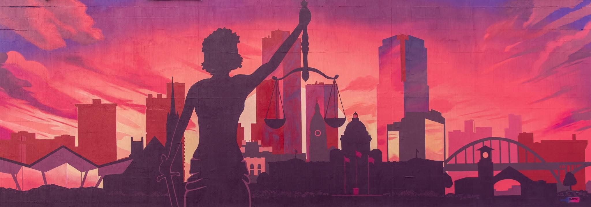 Mural of Lady Justice in silhouette, raising balanced scales in front of the Little Rock skyline, the Arkansas State Capitol, and a river bridge under a pink and purple sunset